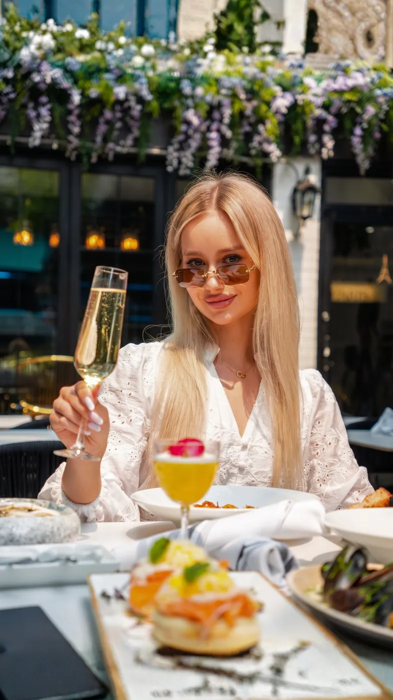 Guest raising a glass of champagne at a sunlit patio table with brunch dishes