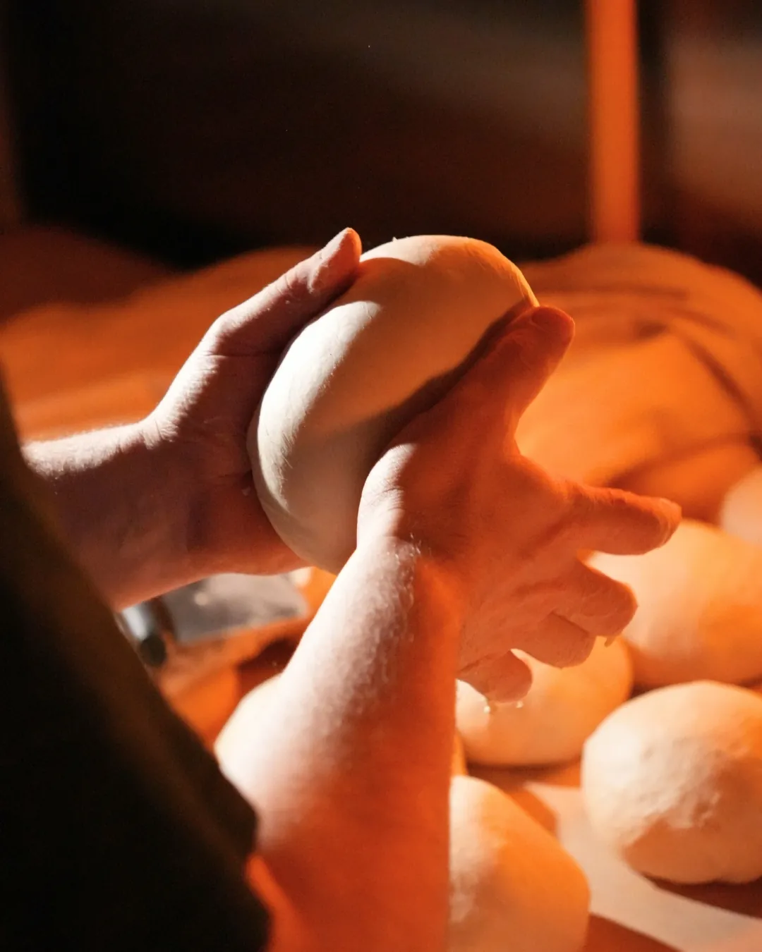 Baker's hands shaping dough under warm light