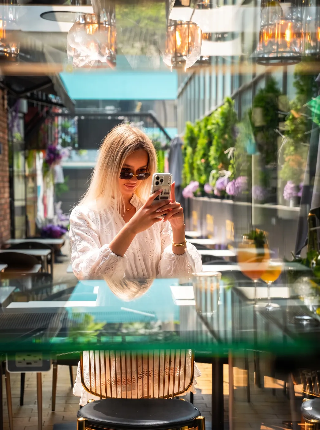 Guest photographing her table on a sunlit restaurant patio, framed through glass